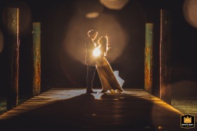 At Pang Ka Bay, Koh Samui, Thailand, a couple has a nighttime photo session on the pier. They are backlit by the photographer, with symmetrical framing.
